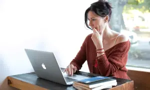 Kobieta przy laptopie, zamyślona, jakby udawała kogoś innego, by zdobyć nowe informacje.