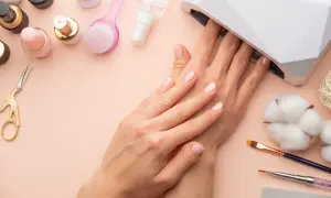 Delikatne paznokcie hybrydowe w ciąży, utwardzane w lampie UV. Wokół akcesoria do manicure: lakiery, pędzelki, nożyczki.