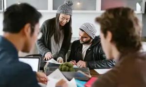 Tre personer diskuterar papper vid ett bord. Kanske planerar de för sitt nya aktiebolag eller enskild firma.