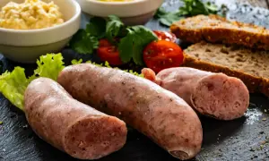 Surowa biała kiełbasa z dodatkami: chlebem, musztardą, chrzanem i pomidorami.