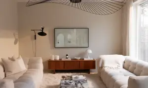 Ett vardagsrum i kall beige ton. Mjuka soffor, en marmorbänk och en träbyrå skapar en lugn atmosfär. En stor taklampa ger ett dramatiskt intryck.