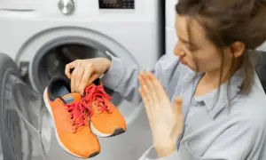 Donna con scarpe arancioni in mano, davanti a una lavatrice aperta. Scopri come lavare le scarpe in lavatrice per farle tornare come nuove.