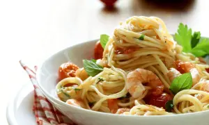 Ein Teller mit köstlichen Spaghetti mit Garnelen, Kirschtomaten und frischem Basilikum, appetitlich angerichtet.
