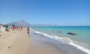 En solig stranddag vid Campofelice di Roccella med folk som badar och kopplar av.