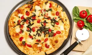 Pyszna pizza z serka wiejskiego, pomidorkami koktajlowymi i bazylią. Obok leżą świeże pomidory i krajalnica do pizzy.