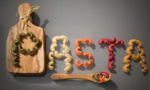 Kolorowy makaron ułożony w napis "PASTA". Kto wymyślił makaron? Może ten, kto ułożył te pyszne kształty na desce i łyżce.