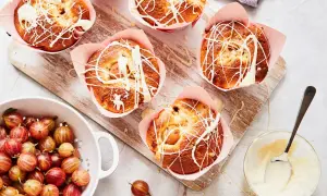 Frisch gebackene Stachelbeer Muffins mit weißer Schokoladenglasur, daneben eine Schüssel voller Stachelbeeren.