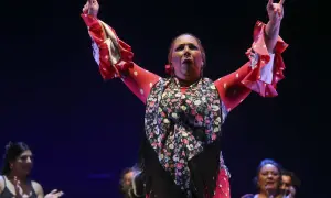 Raquel Heredia, con brazos en alto, luce un traje rojo de lunares blancos y un mantón floral.