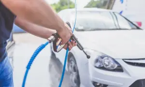 Mężczyzna myje biały samochód samą wodą pod ciśnieniem.