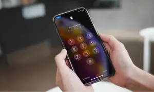 Dłonie trzymające iPhone'a z ekranem blokady i klawiaturą numeryczną.