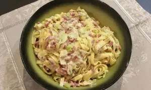 Un plat de tagliatelle poireaux crémeuses avec des lardons, servi dans un bol vert.