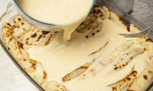 Naleśniki z serem w naczyniu żaroodpornym, zalewane kremowym sosem.