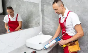 Remont łazienki: fachowiec nakłada silikon sanitarny wokół umywalki. Dowiedz się, ile powinien schnac silikon sanitarny.