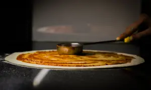 Ręka rozprowadza sos pomidorowy na cieście, tworząc idealny zaczyn na pizzę.