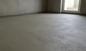 Świeżo wylana posadzka betonowa w pustym pomieszczeniu. Czekamy, aż beton wyschnie, zanim będziemy mogli kontynuować prace.