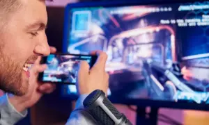 Mężczyzna gra w grę na telefonie, która jest wyświetlana na monitorze komputera.