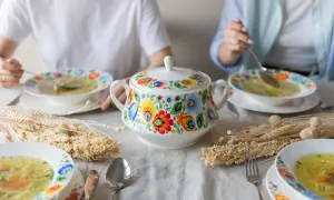 Stół z miskami zupy, ozdobionymi tradycyjnymi wzorami, i ozdobnymi kłosami.