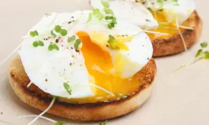 Dos deliciosos huevos poche sobre tostadas inglesas, adornados con brotes verdes y pimienta. La yema dorada fluye, invitando a un bocado perfecto.