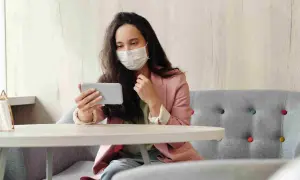 Donna con mascherina guarda il telefono, forse per informarsi sulla situazione, mostrando una certa paura dei virus.