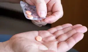 Dłoń przyjmuje pomarańczową tabletkę na cholesterol z blistra.