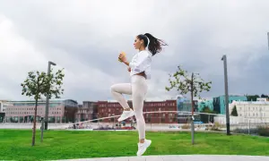 Kobieta w białym stroju sportowym wykonuje bieg w miejscu na tle miejskiego krajobrazu.