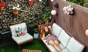 Mujer relajándose en un patio decorado para **decorar patios pequeños con poco dinero**. Flores, luces y muebles crean un oasis acogedor.