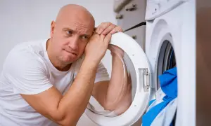 Zmartwiony mężczyzna opiera głowę o otwarte drzwi pralki Whirlpool, która wyświetla błąd F05.