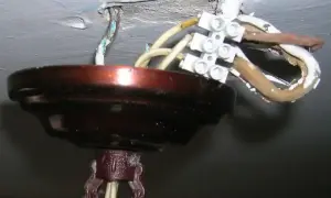 Podłączenie żyrandola: 3 kable z sufitu połączone w kostce. Widoczna metalowa osłona i fragment mocowania.