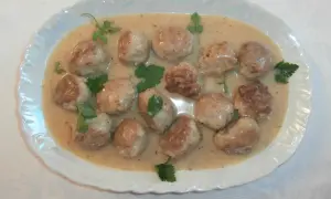 Pyszne pulpety w sosie własnym, udekorowane natką pietruszki, prezentują się apetycznie na białej, ozdobnej tacy.