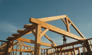Budowa domu z drewna, gdzie widoczna jest adaptacja projektu gotowego. Drewniana konstrukcja szkieletowa na tle błękitnego nieba.