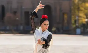 Bailarina de flamenco con un vestido blanco y negro, flor roja en el pelo, moviendo sus brazos al ritmo rumba.