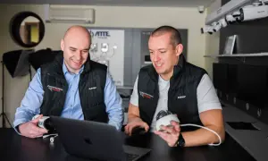 Dwóch mężczyzn omawia systemy monitoringu. Jeden trzyma kamerę, drugi patrzy na laptopa, planując zdalny monitoring.