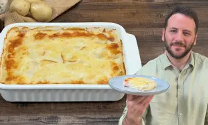 Un uomo sorride mostrando una porzione di parmigiana di patate appena sfornata, dorata e filante.
