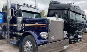Deux camions américains, un bleu et un noir, brillent sous un ciel couvert. Le bleu, un Peterbilt, arbore des touches orange et beaucoup de chrome.
