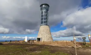 Nowoczesna wieża na Śnieżniku, z kamienną podstawą i szklaną częścią, góruje nad krajobrazem.