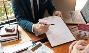 Biznesmen z długopisem wskazuje na umowę kupna. Obok leży model domu, klucz i kalkulator. To pokazuje, co to jest wibor w kontekście kredytu hipotecznego.
