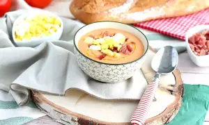 Schüssel mit Gazpacho, garniert mit Ei und Schinken. Daneben sind Tomaten, Brot und weitere Zutaten für kalte Tapas.
