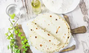 Domowy tortilla przepis: świeżo upieczone placki, mąka, olej i woda na drewnianej desce.
