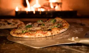 Pizza na łopacie w piecu opalanym drewnem, z płomieniami w tle.