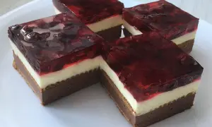 Cztery kawałki ciasta bez pieczenia z warstwami czekolady, kremu i galaretki z wiśniami.