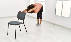 Femme pratiquant le yoga sur chaise, se penchant en avant pour étirer son dos, mains posées sur le dossier du siège.