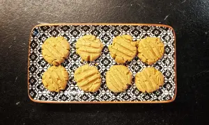 A rectangular plate with a black and white floral pattern holds eight golden-brown kekse ohne zucker.