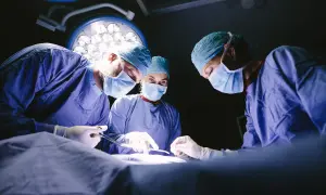 Trois médecins spécialistes en blouse bleue, masqués, concentrés sur une opération sous les lumières vives du bloc opératoire.