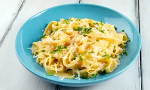 Un piatto di pasta burro e parmigiano, condita con prezzemolo fresco, servita in una ciotola blu su un tavolo di legno.
