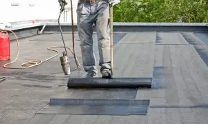 Arbeiter repariert ein Blechdach mit einem Brenner und Bitumenbahnen.
