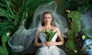 Kirsten Dunst w białej sukni ślubnej leży w wodzie wśród lilii wodnych i trawy. Scena przypomina kadr z jednego z jej filmów.