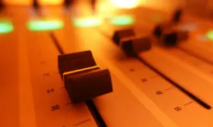 Suwaki miksera audio, oświetlone ciepłym, pomarańczowym światłem. To miejsce, gdzie rodzi się dźwięk.
