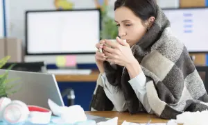 Femme emmitouflée dans une couverture, buvant une tasse de thé, peut-être à cause d'une mauvaise température ambiente.