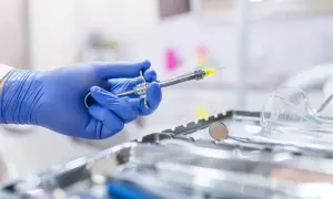 Main d'un dentiste en gant bleu tenant une seringue pour une piqûre aiguille sans saignement. Instruments médicaux en arrière-plan.
