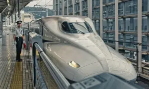 Na peronie stoi konduktor obok najszybszej kolejki na świecie, Shinkansen, gotowej do podróży.